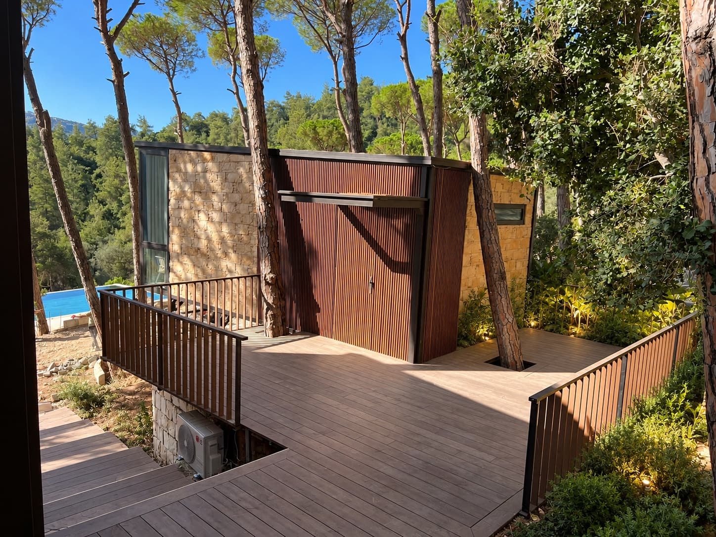 A stone and timber bungalow on its deck among the pines, with the pool below