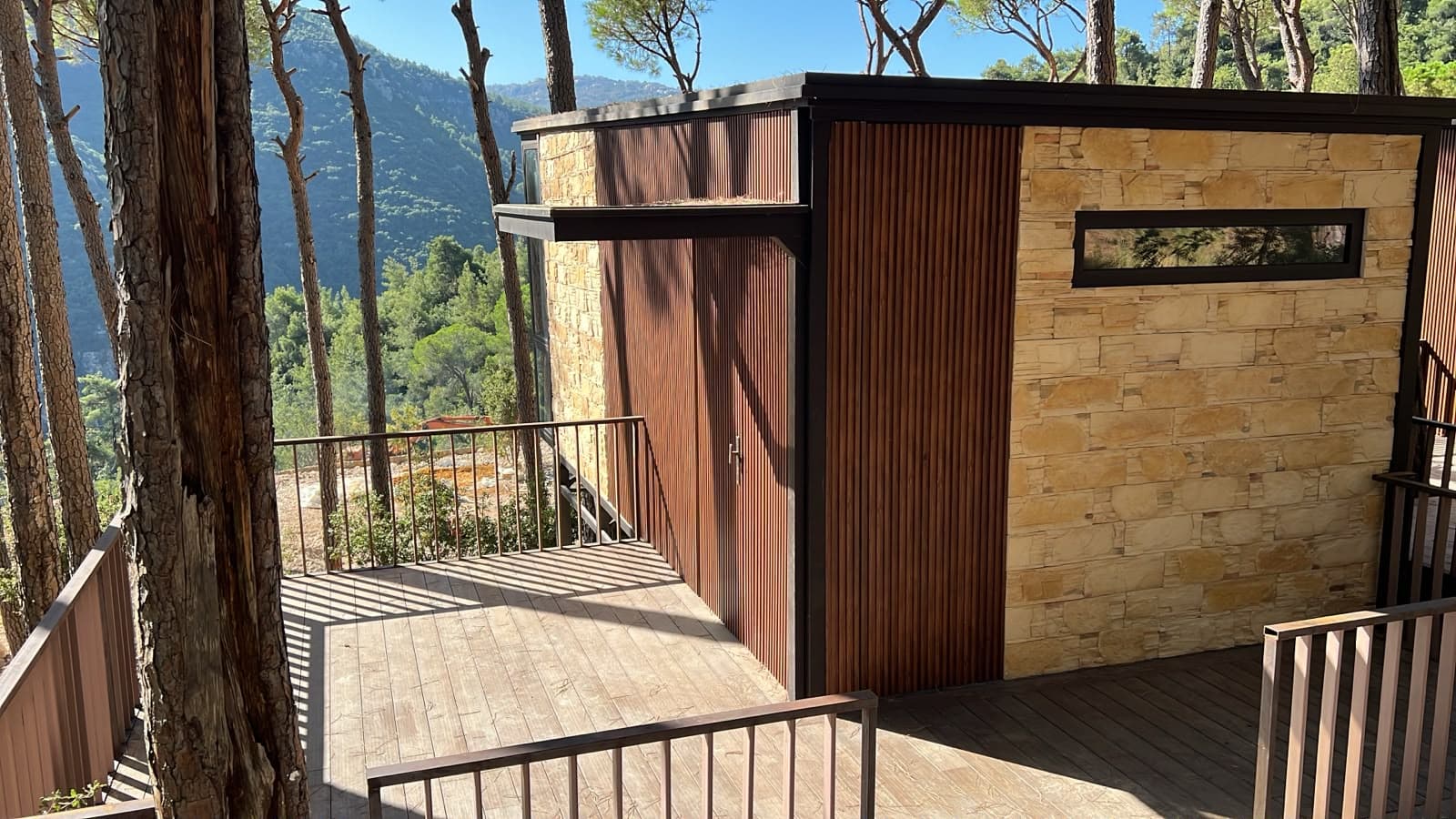 Pinea Terra, a stone and timber bungalow on its deck, with pine trunks in front and the mountains behind