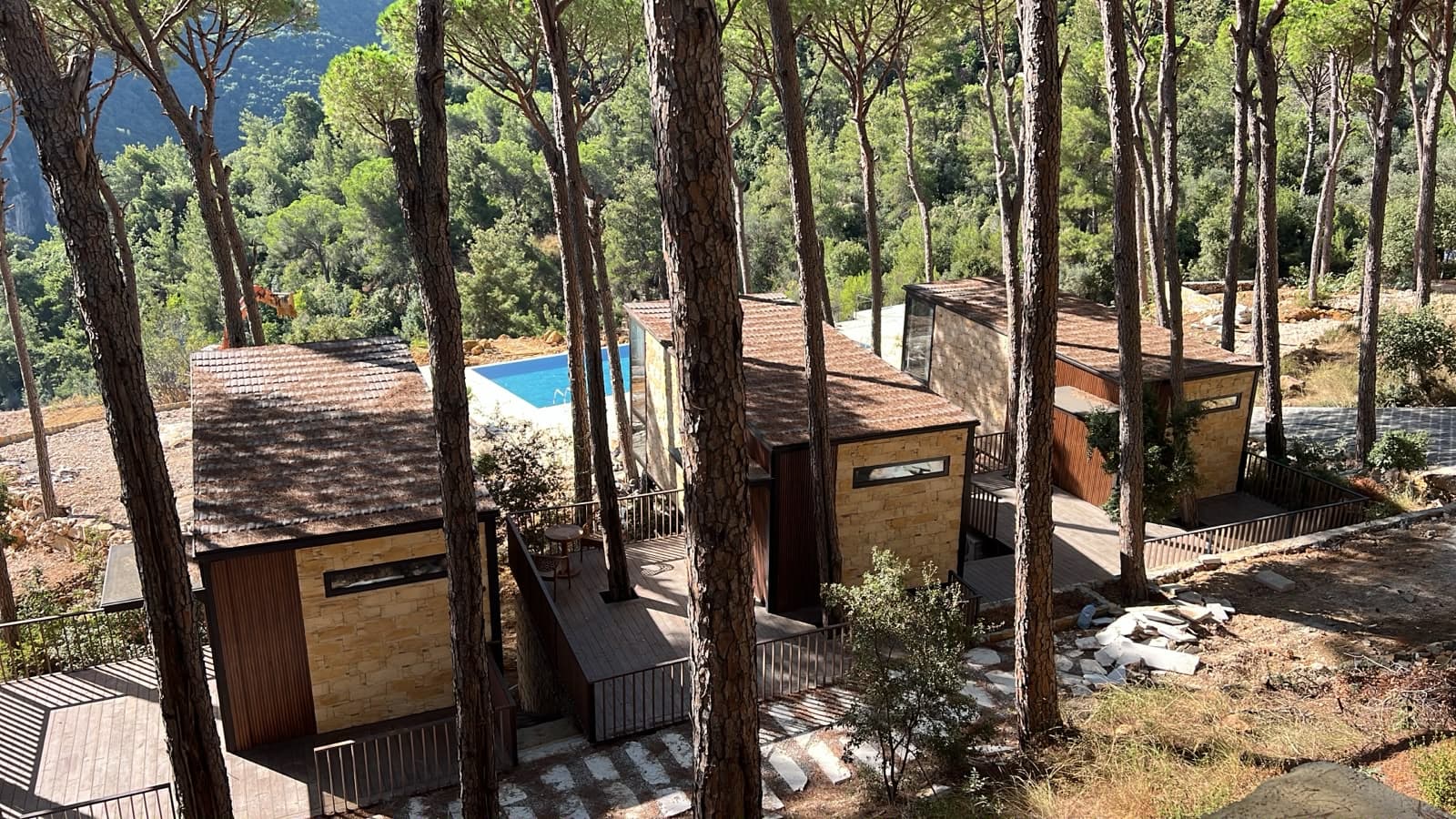 The three bungalows seen from above, stepping down through the pines toward the pool