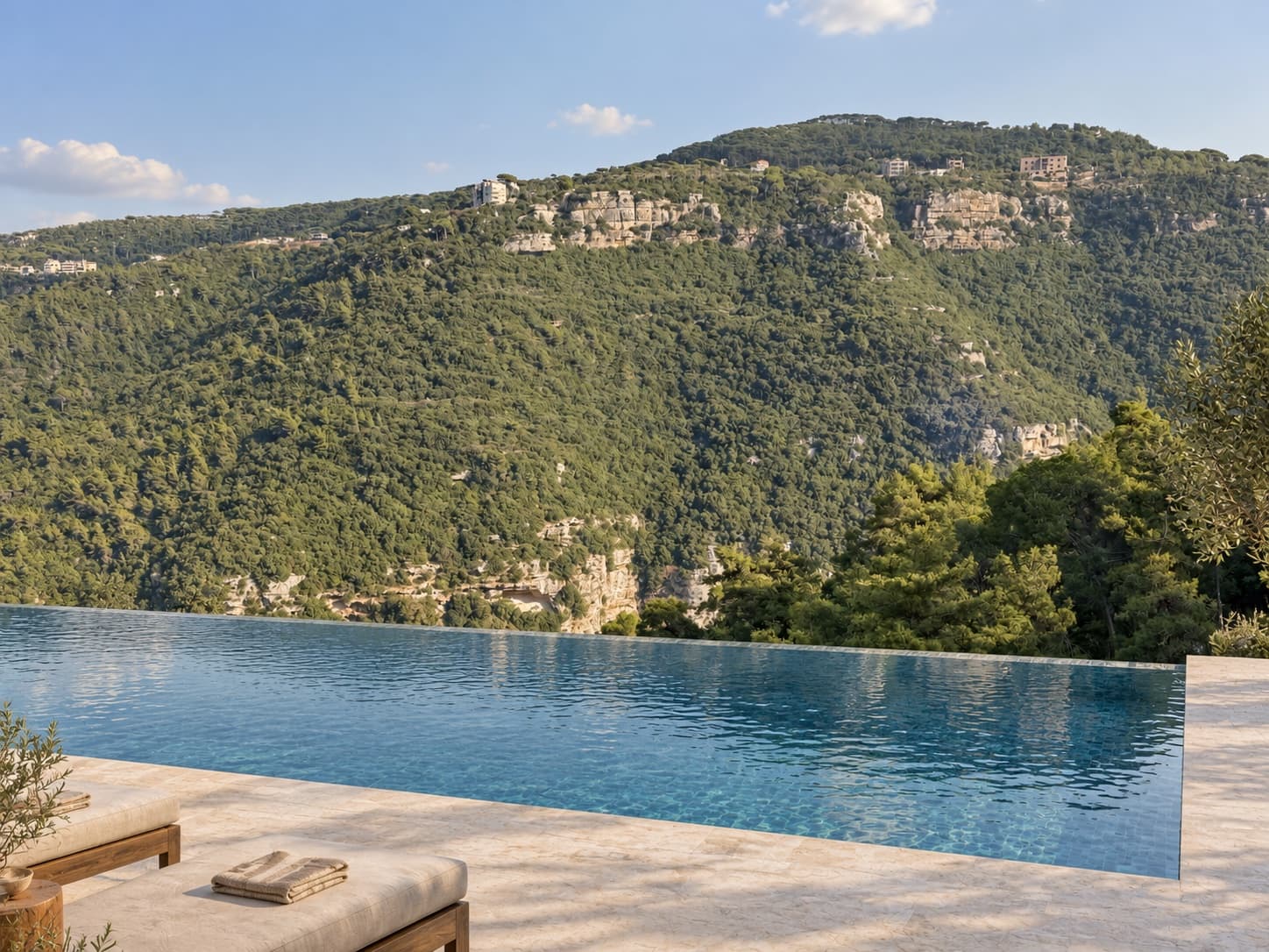 Sunbeds with folded towels beside the infinity pool, facing the forested cliffs across the valley